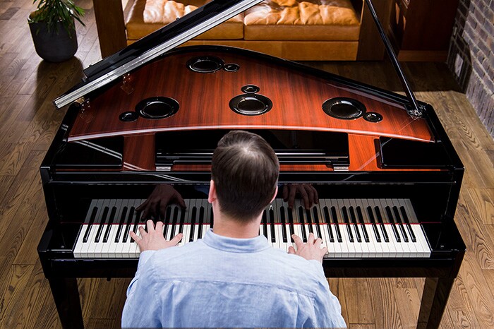 Behind view of man playing hybrid piano with speakers under the lid.
