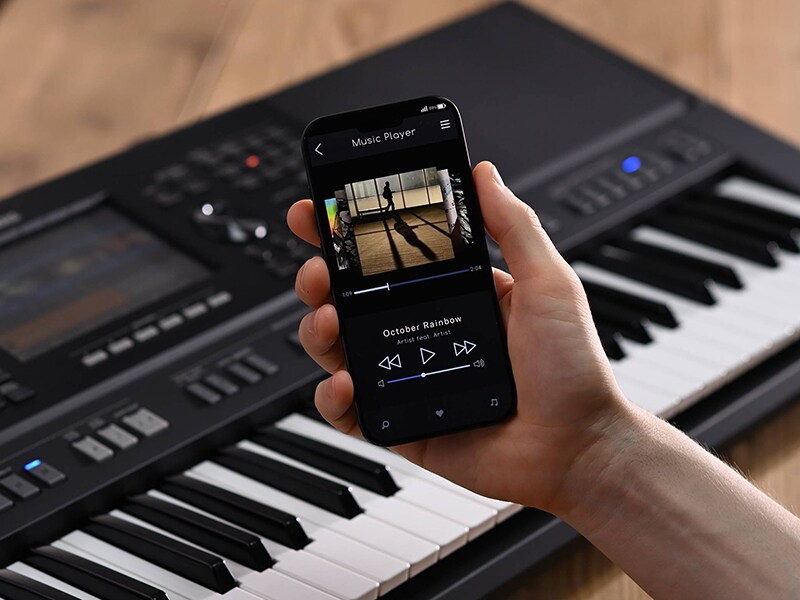 Station de travail arrangeur Yamaha PSR-SX920 et une main tenant un téléphone intelligent affichant l'écran d'un lecteur de musique