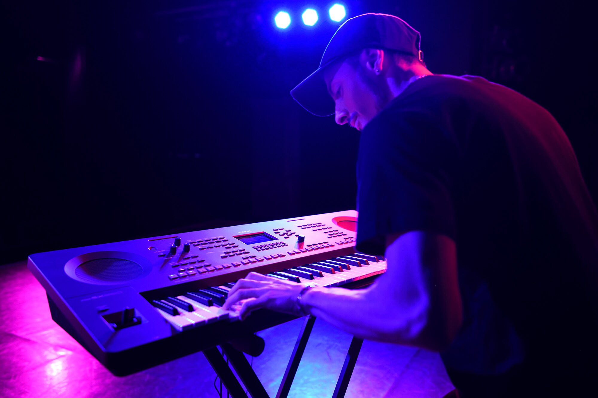 Une personne jouant sur un clavier arrangeur Yamaha posé sur un support sous les projecteurs d'une scène