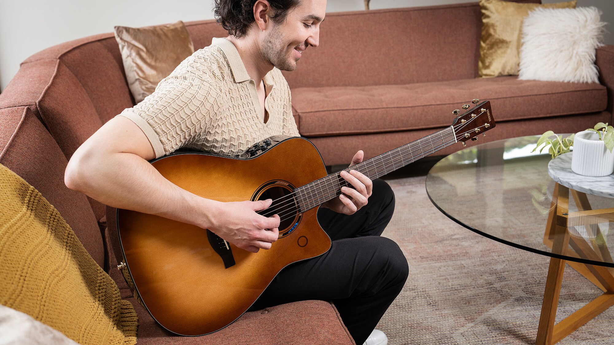 Un homme assis sur un sofa dans le salon jouant d'une guitare acoustique TAG3 C