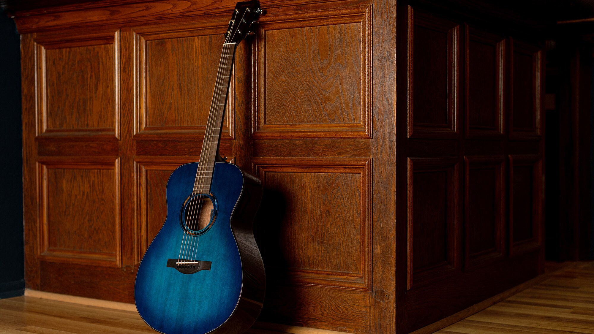 Une guitare acoustique TAS1E debout contre un mur brun à l'intérieur