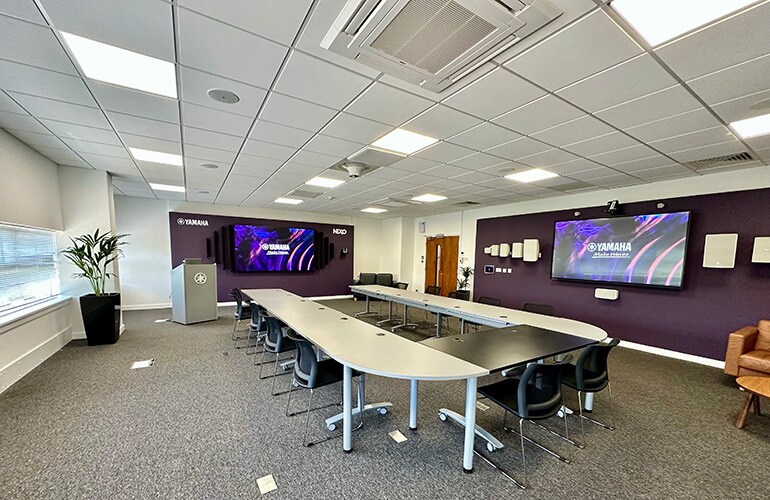 Centre de formation de Milton Keynes avec tables, chaises, écran d'affichage et équipement audio.