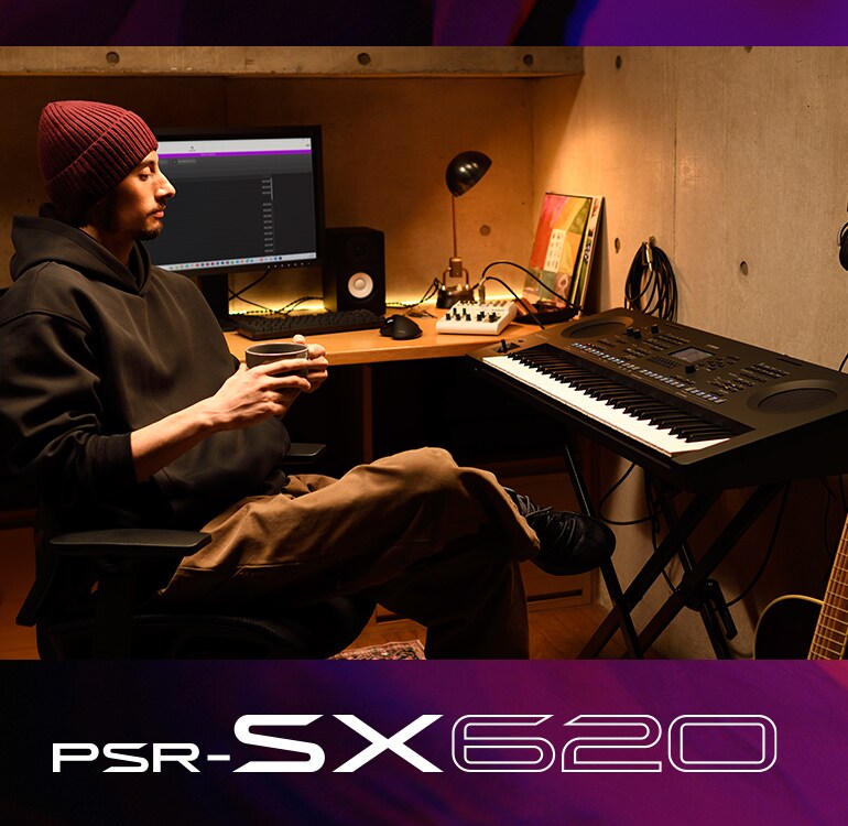 Une personne assise devant un clavier PSR-SX dans un studio maison, buvant du café.