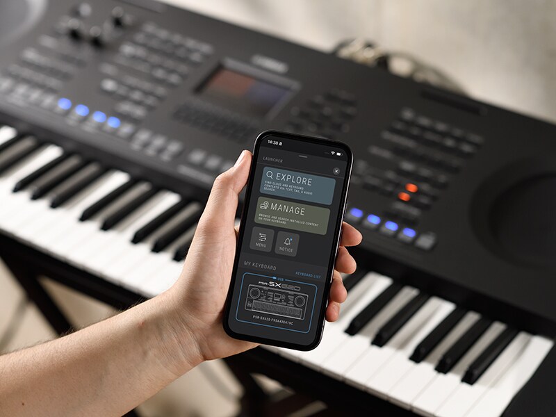 Le PSR-SX920 et une main tenant un téléphone intelligent qui affiche l'écran d'un lecteur de musique.