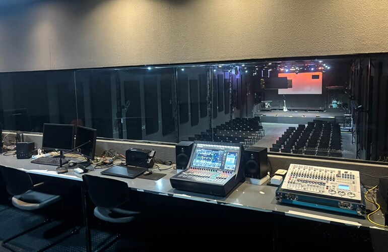 Régie du centre de formation de São Paulo avec consoles de mixage numériques, écrans et baies d'équipement audio.