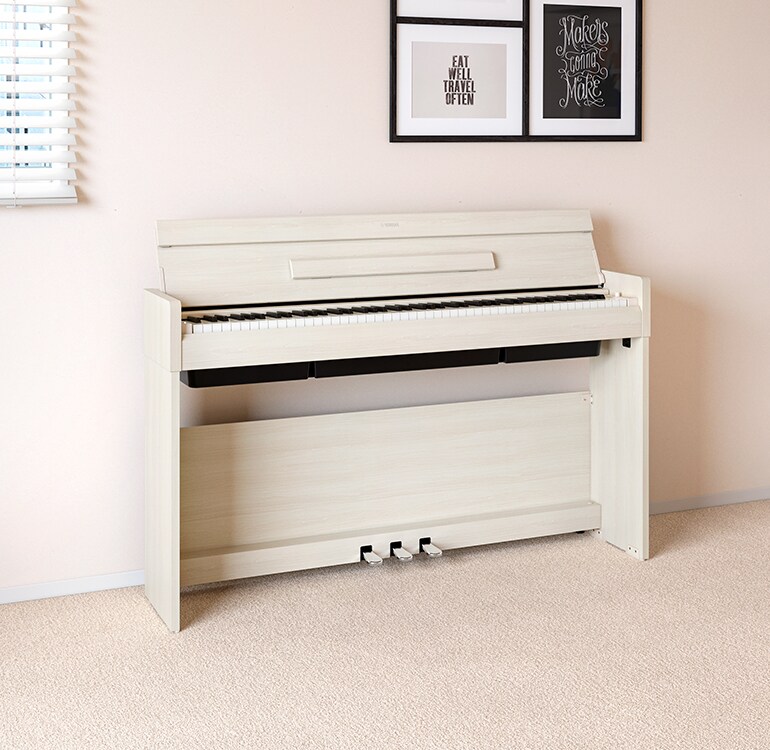 Un salon mettant en vedette un piano ARIUS en bouleau blanc installé à côté d'étagères murales sur lesquelles sont posés des lampes et un diffuseur, s'intégrant harmonieusement à l'intérieur.