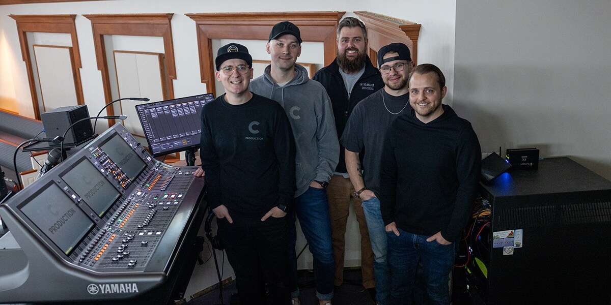 Des membres de l'équipe audio de Christ Community Chapel debout à côté d'une console de mixage Yamaha RIVAGE PM.