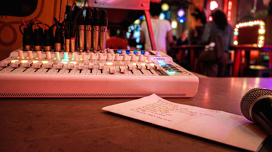 Console de mixage MGX16V de Yamaha installée à la régie de façade, avec un microphone et la liste des morceaux du concert visibles.