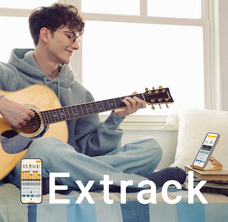 Un homme s'exerce à la guitare assis sur le sofa, tout en s'accompagnant de l'application de pratique musicale Extrack