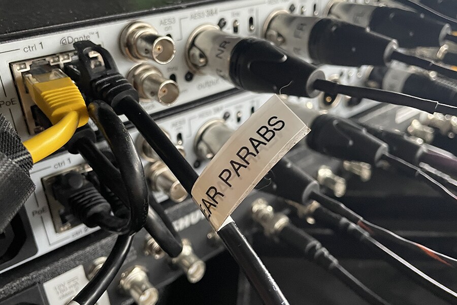 Gros plan des connexions de l'équipement audio montrant les câbles réseau Dante et les sorties des micros paraboliques