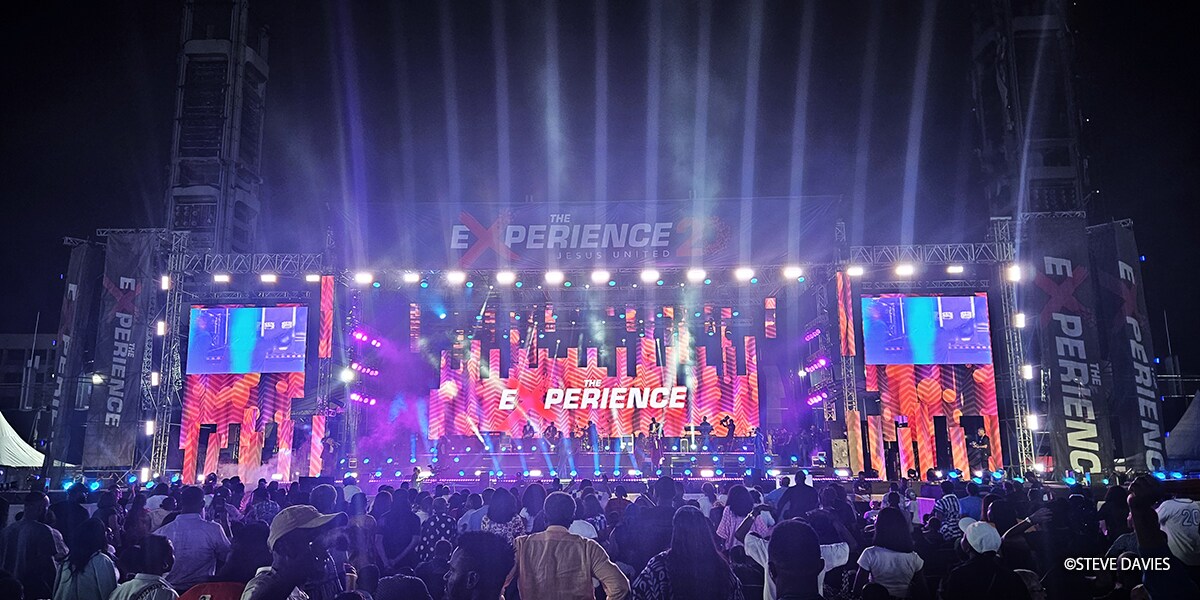 Vue d'ensemble de The Experience 2025 à Lagos, au Nigeria, montrant une grande scène extérieure avec éclairage et écrans vidéo où des artistes se produisent devant une foule de fidèles lors de l'événement annuel de musique gospel.